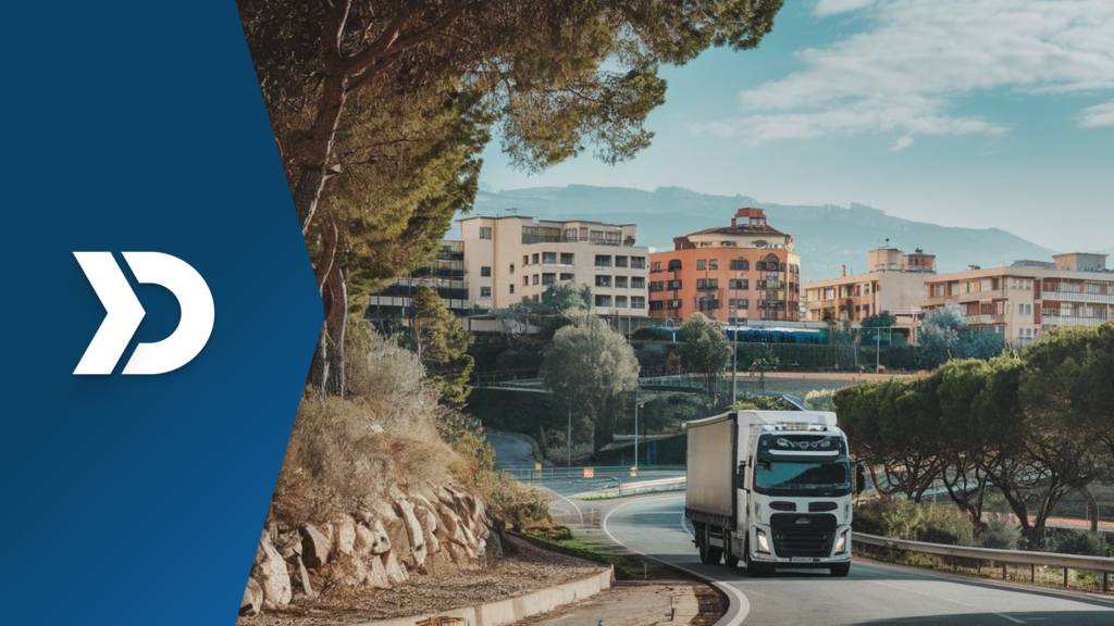 A white semi-truck driving on a curved road near a scenic urban area, symbolizing the role of mobile telematics in tracking and reducing vehicle carbon emissions.
